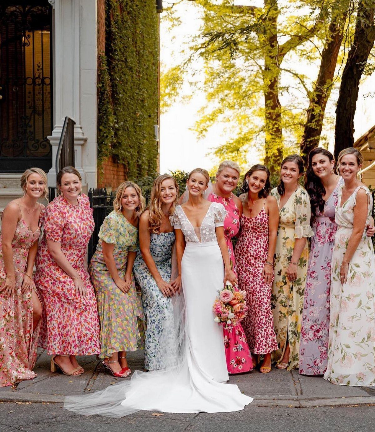 Bridesmaids in various floral patterned dresses standing with a bride in a white wedding gown.