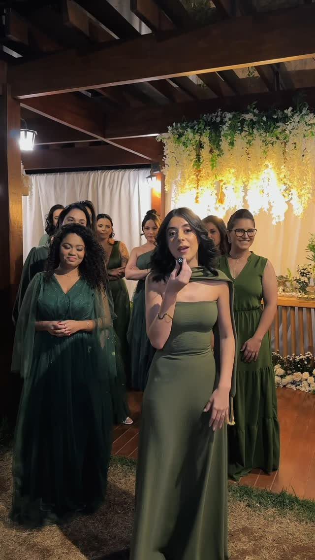 Bridesmaids standing together wearing various styles of dark green dresses during an outdoor evening event.