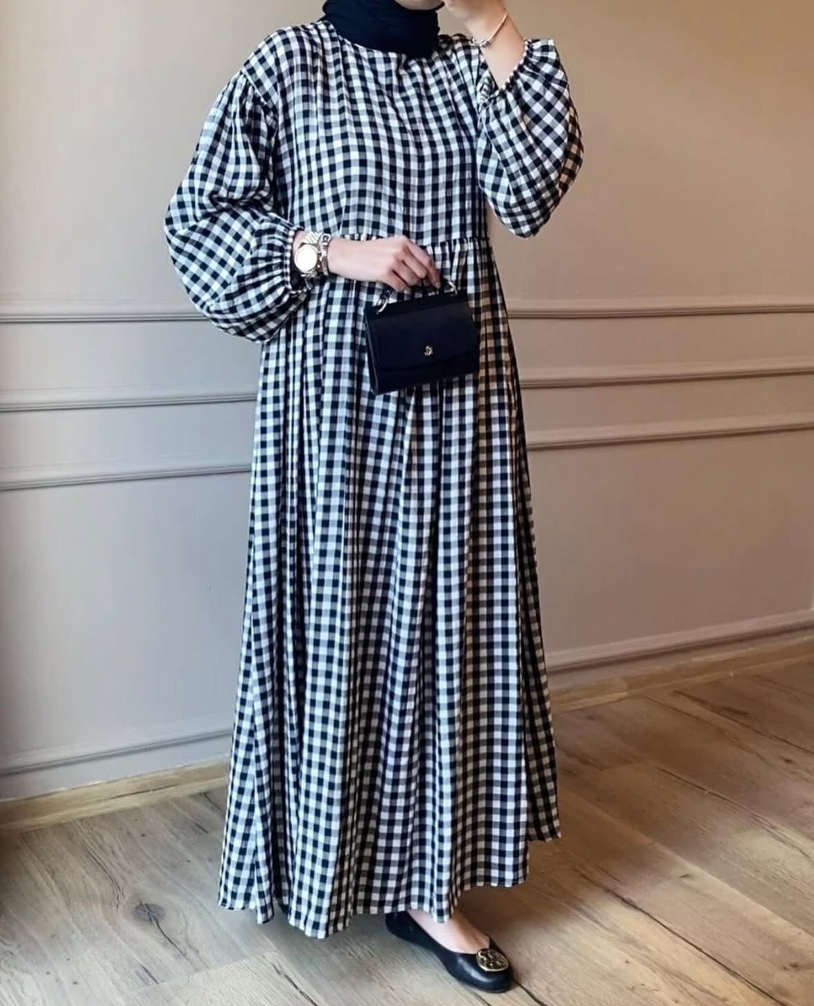 A person wearing a black and white gingham maxi dress with a black hijab and handbag.