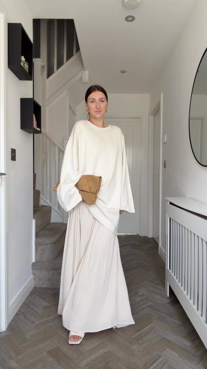 Woman in a cream long-sleeved top and matching long maxi skirt standing in a hallway.
