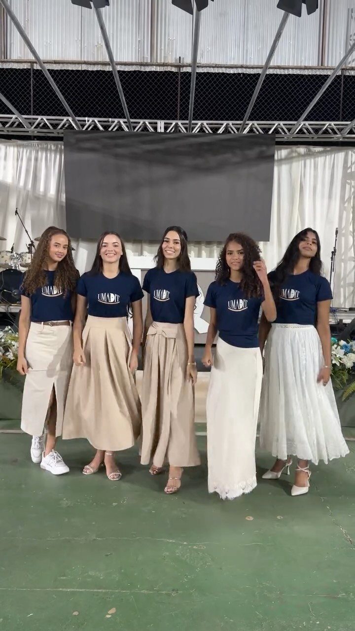 Five women posing in matching navy t-shirts and long, flowing skirts in neutral tones.