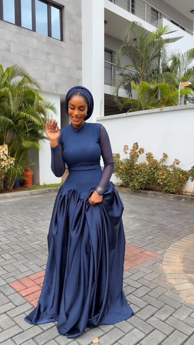 Woman in a navy blue high neckline maxi dress with a voluminous skirt and matching headwrap.