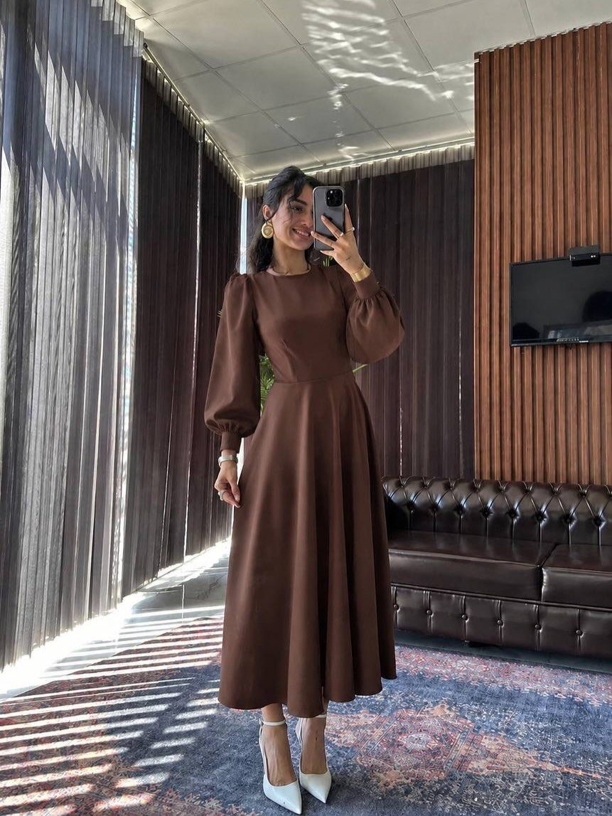 Woman in a chocolate brown midi dress with voluminous puff sleeves taking a mirror selfie.