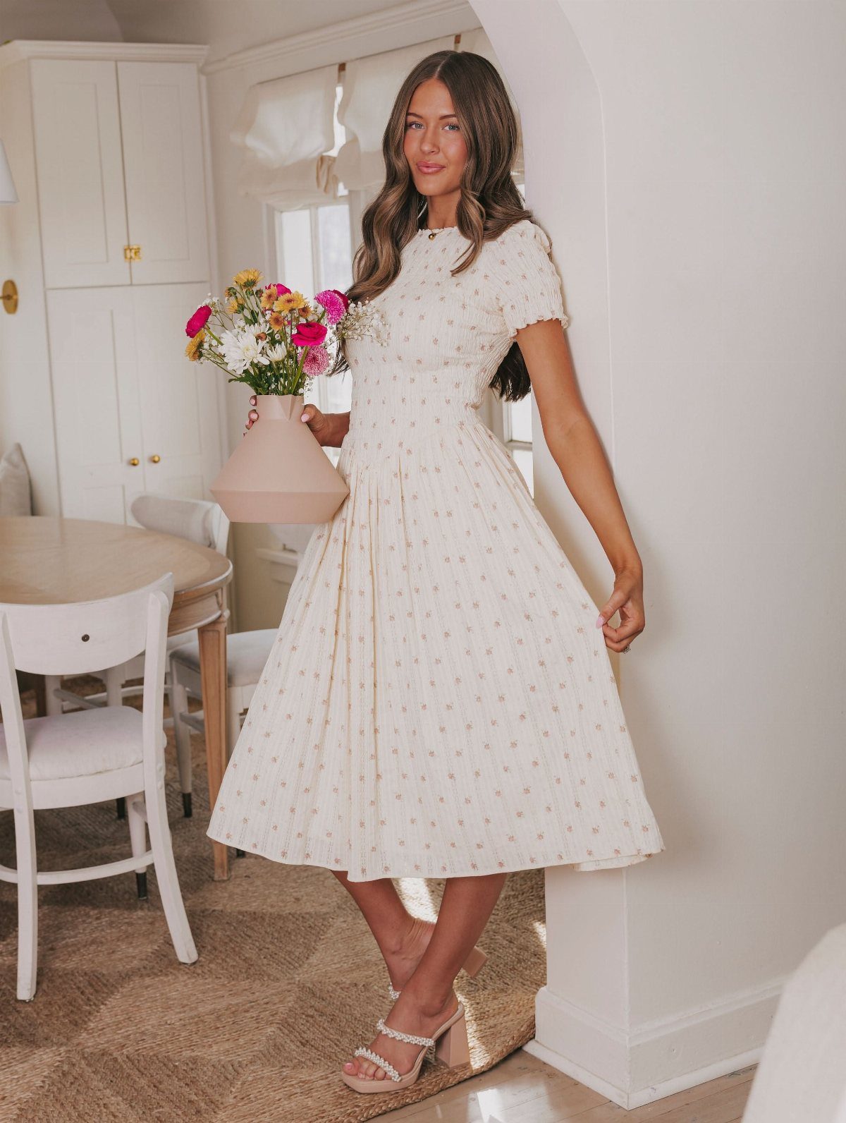 Woman in a cream floral midi dress with a smocked bodice holding colorful flowers.