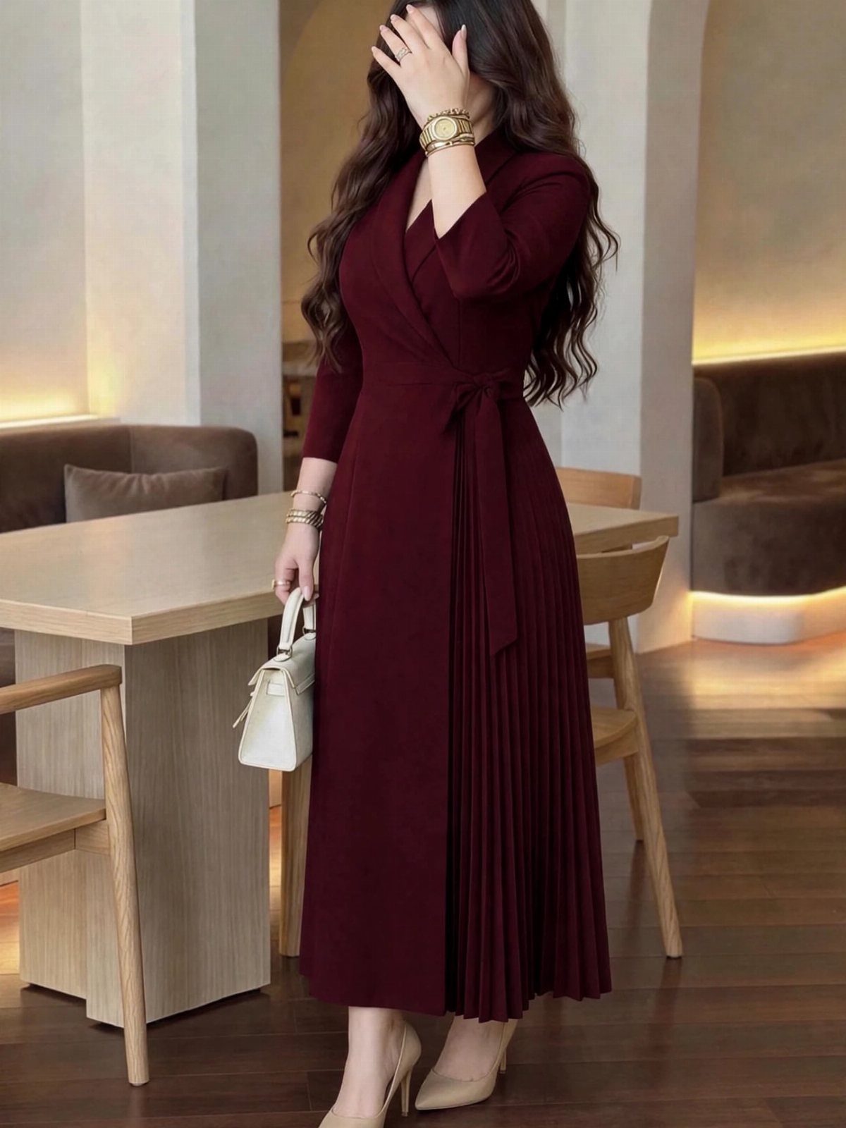 Woman in a burgundy wrap dress with a pleated skirt standing in a modern room.
