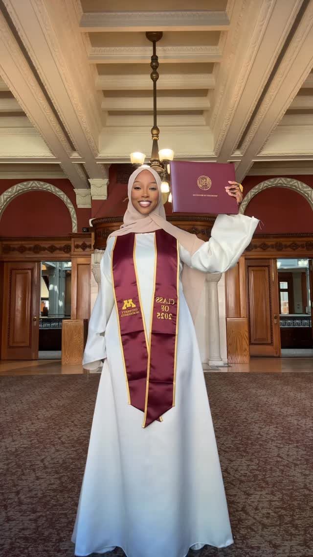 A woman in a white A-line dress and hijab holding a graduation diploma.