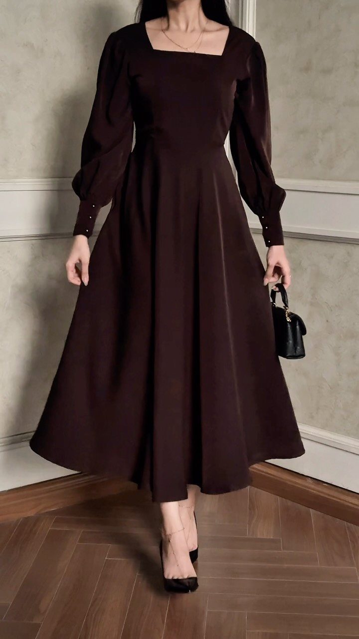 A person wearing a dark brown midi-length A-line dress with long sleeves and a square neckline.