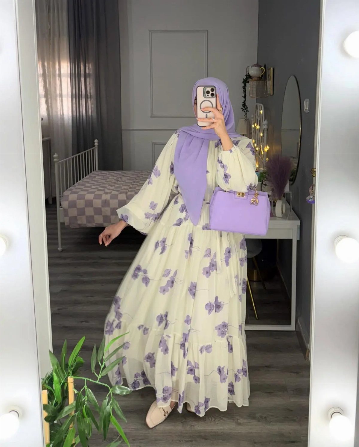 Woman in a floral cream maxi dress and lavender hijab posing for a mirror selfie.