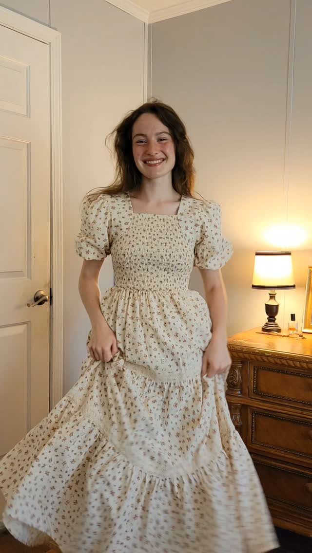 A smiling young woman wearing a long, cream-colored floral print modest summer dress with puff sleeves.