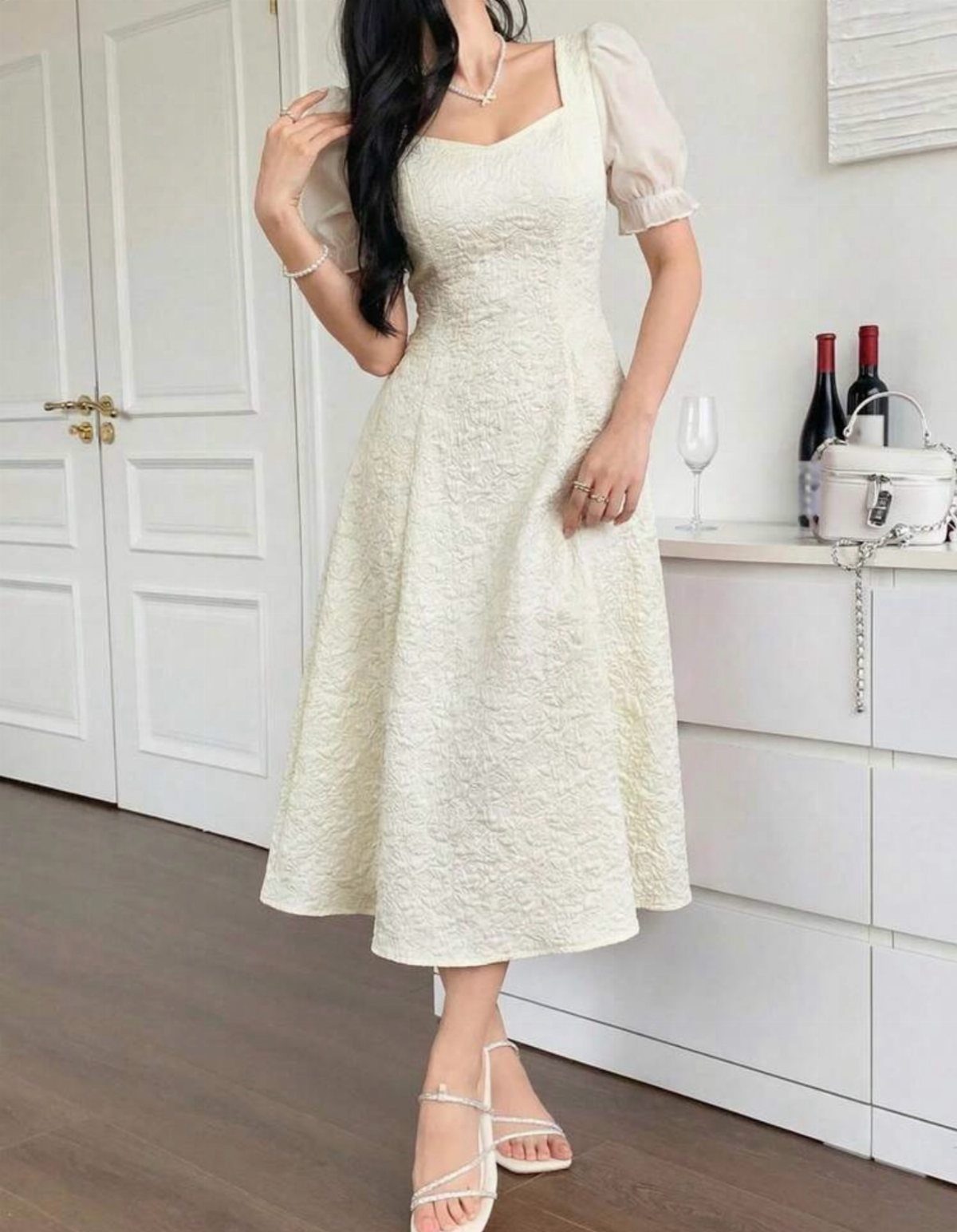 Woman wearing a white textured midi dress with short puff sleeves standing in a bright room.