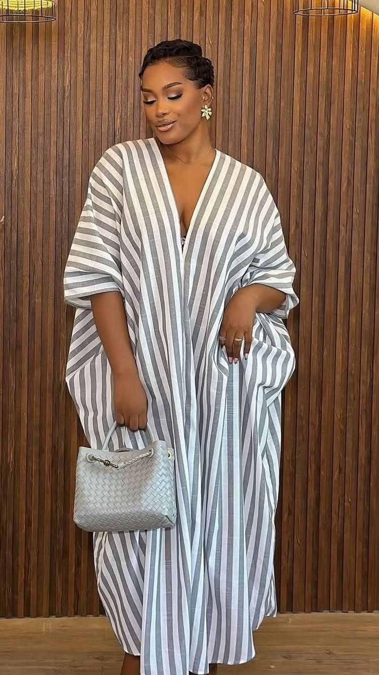 Woman in a striped, loose-fitting kaftan dress holding a small grey handbag.