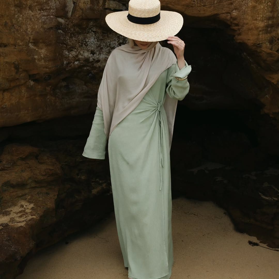 A person in a long green dress and beige headscarf wearing a wide-brimmed straw hat.