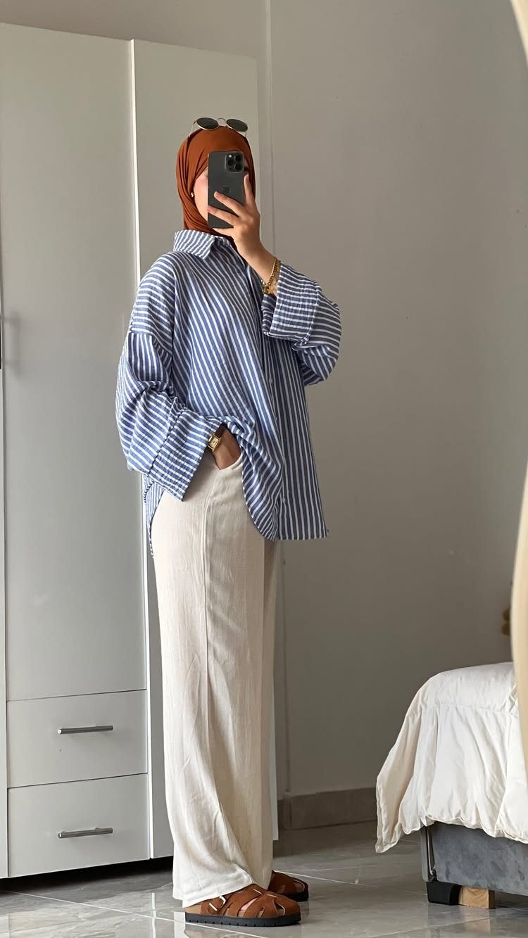 Person in striped shirt, cream trousers, and orange hijab taking a mirror selfie.