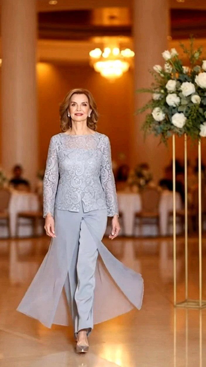 Woman in a light blue lace top and flowing trousers walking through a ballroom.