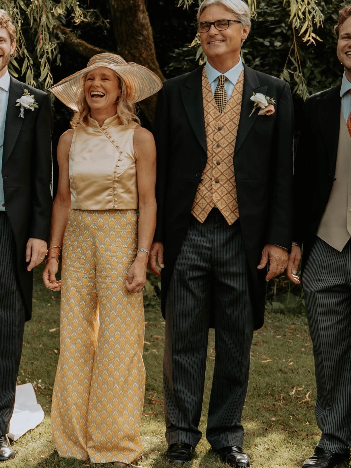 Woman in gold satin top and yellow patterned wide-leg trousers smiling outdoors.