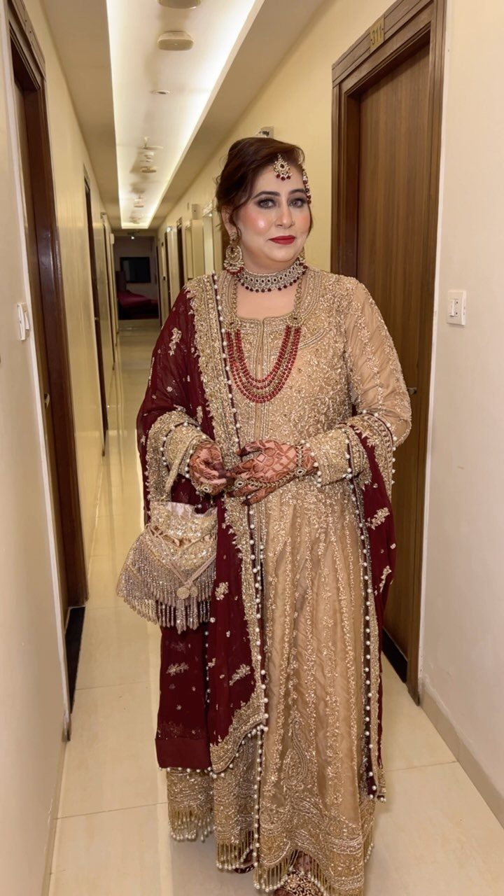 Woman in gold embroidered traditional South Asian attire and red dupatta standing in a hallway.