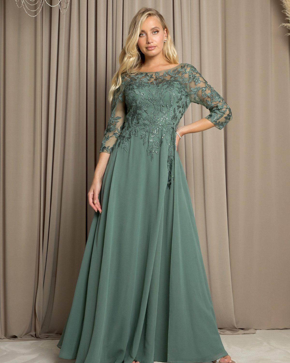 A woman wearing a long sage green lace dress with sheer embroidered sleeves.