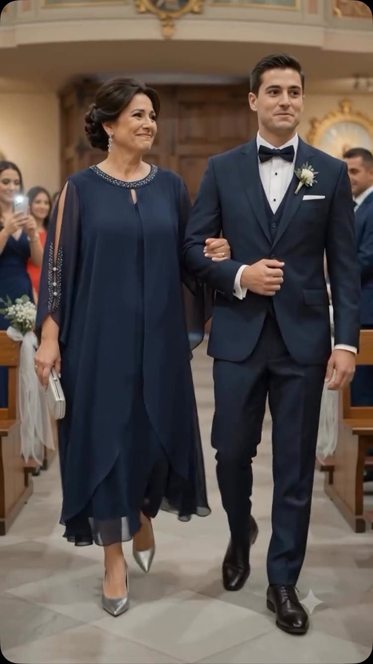 A woman in a navy blue dress walks arm-in-arm with a man in a suit down a church aisle.