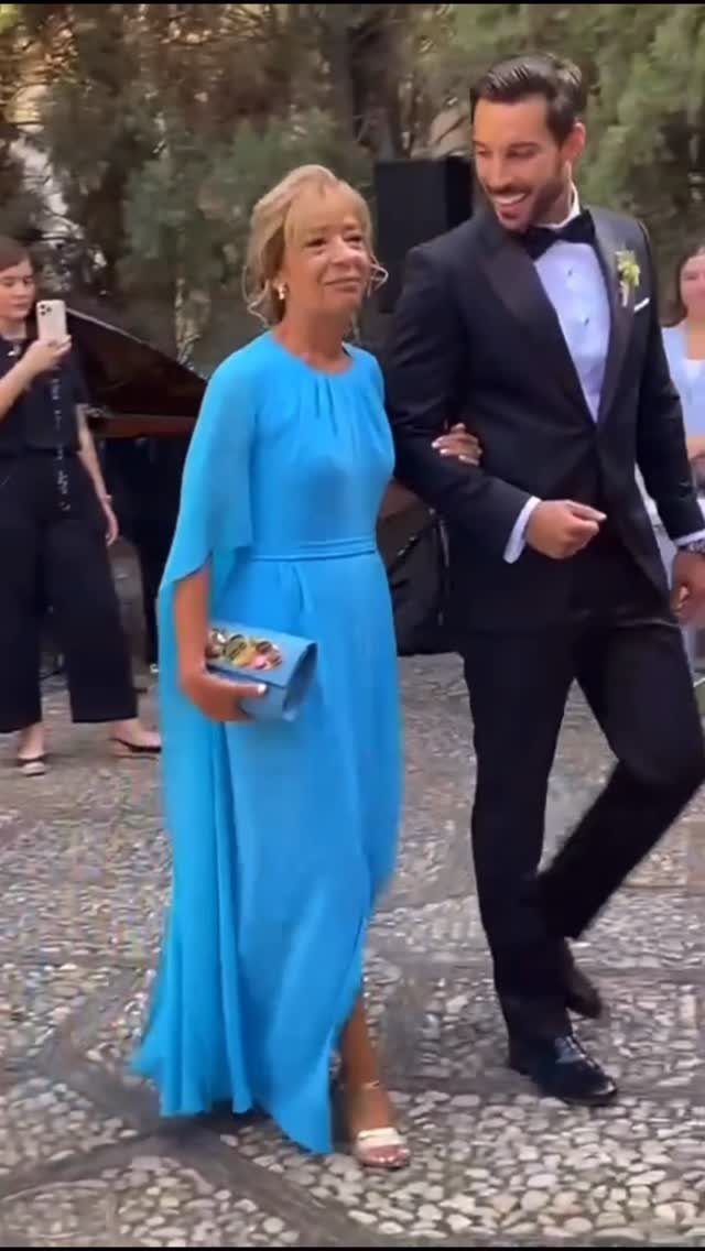 A woman in a blue dress walking arm-in-arm with a man in a tuxedo.