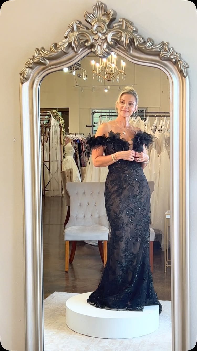 A woman posing in a black sequined floor-length gown with feather trim in a boutique.