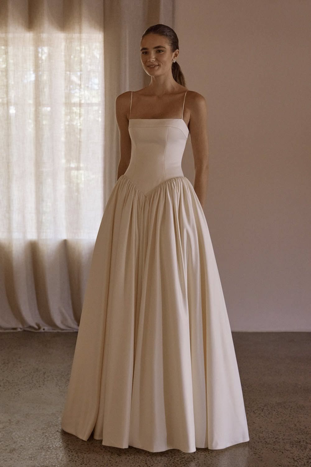 Woman in a cream sleeveless gown with a drop waist and pleated skirt.