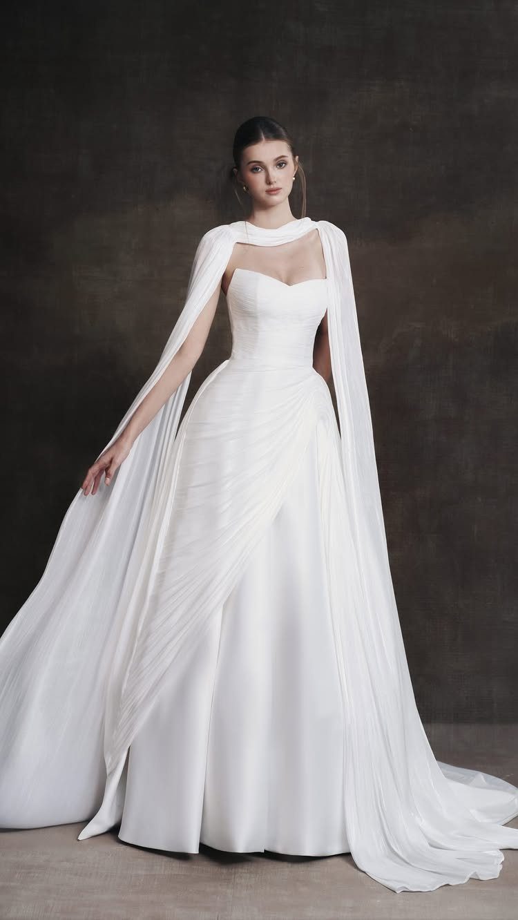 Woman wearing a white pleated wedding dress with a flowing A-line skirt and long sheer sleeves.