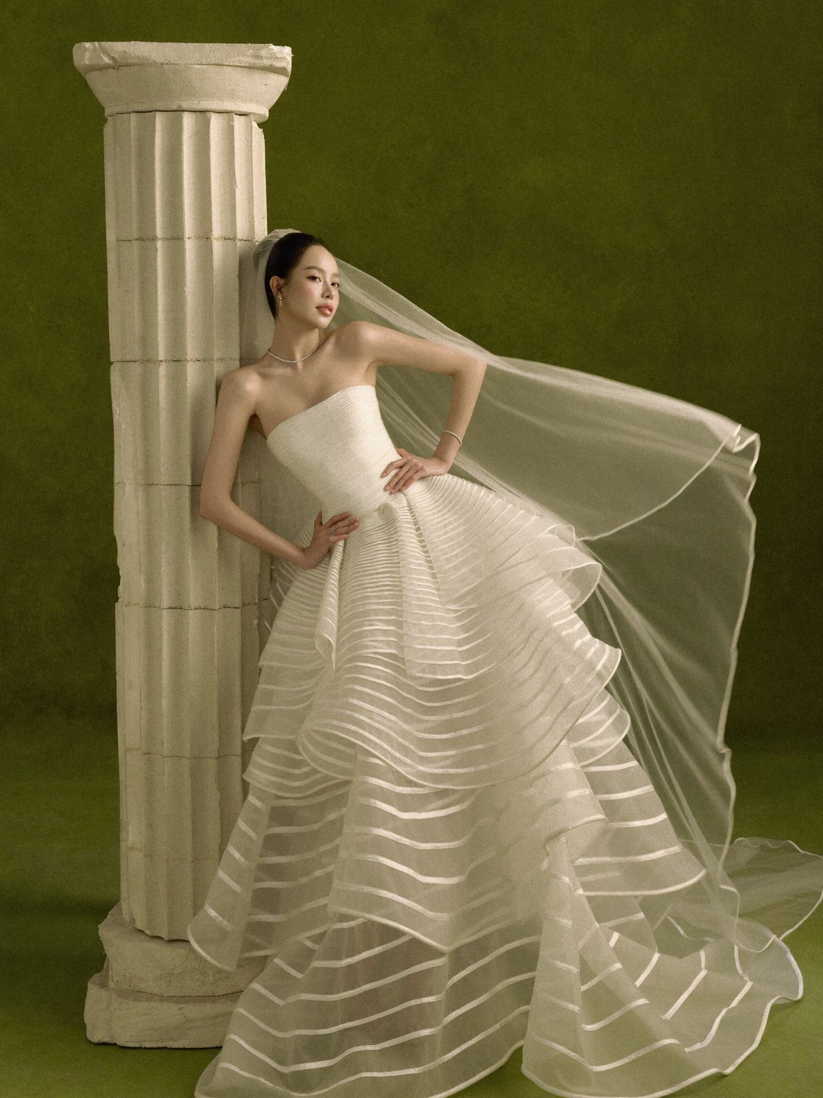 Woman in a white strapless pleated ball gown posing next to a classical column.
