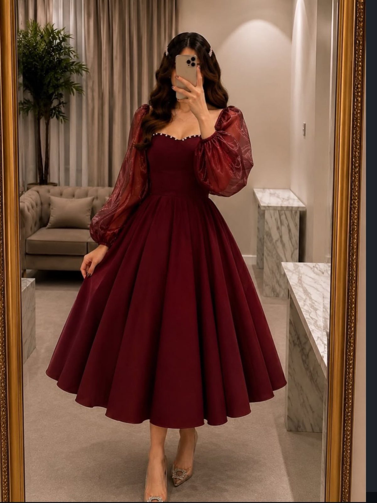 Woman posing in a mirror wearing a plum satin dress with large sheer puff sleeves.