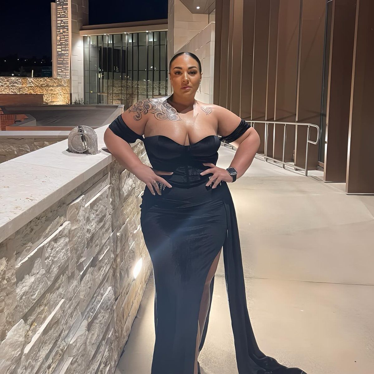 Plus size woman posing in a black off-the-shoulder maxi dress with a high slit.