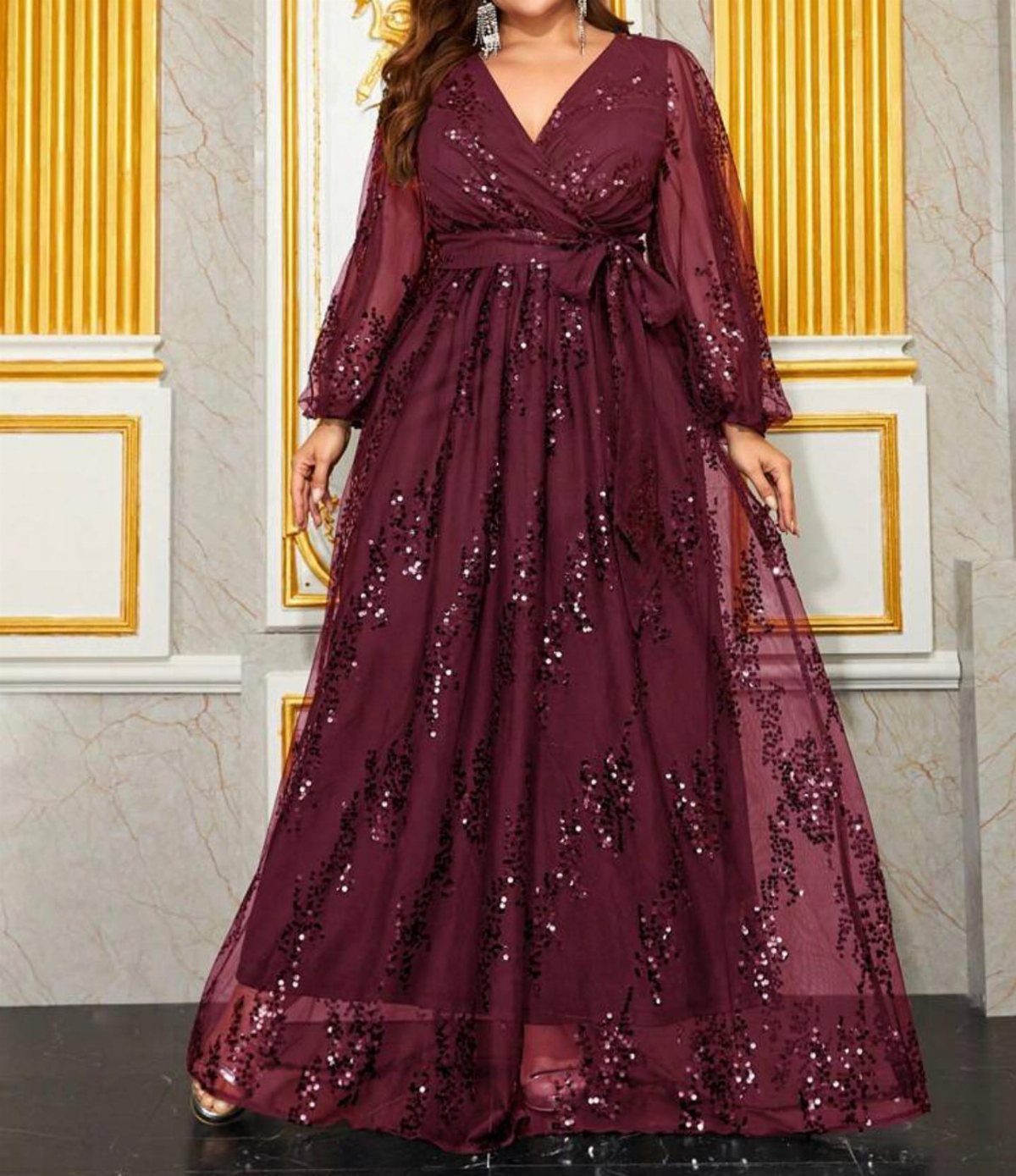 A woman posing in a burgundy sequined maxi dress with long sheer sleeves.