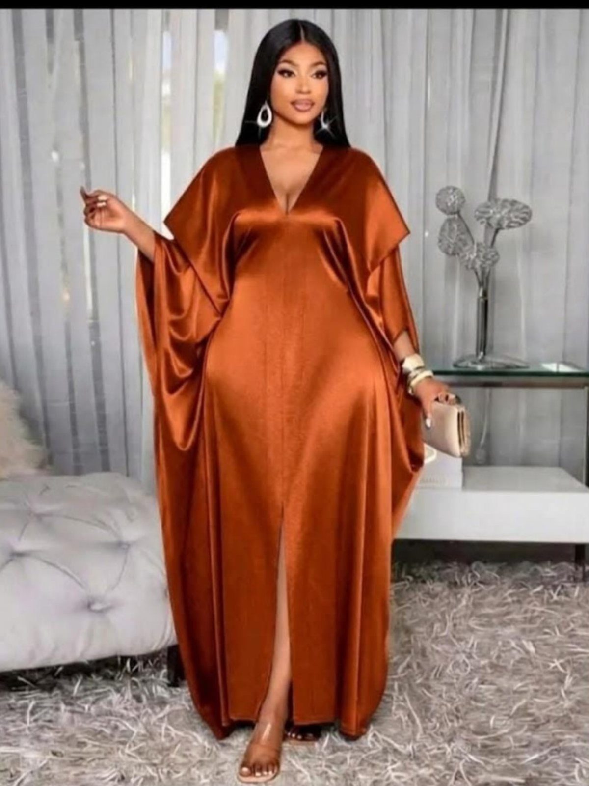 A woman wearing a long, copper satin formal dress poses in a bright room.