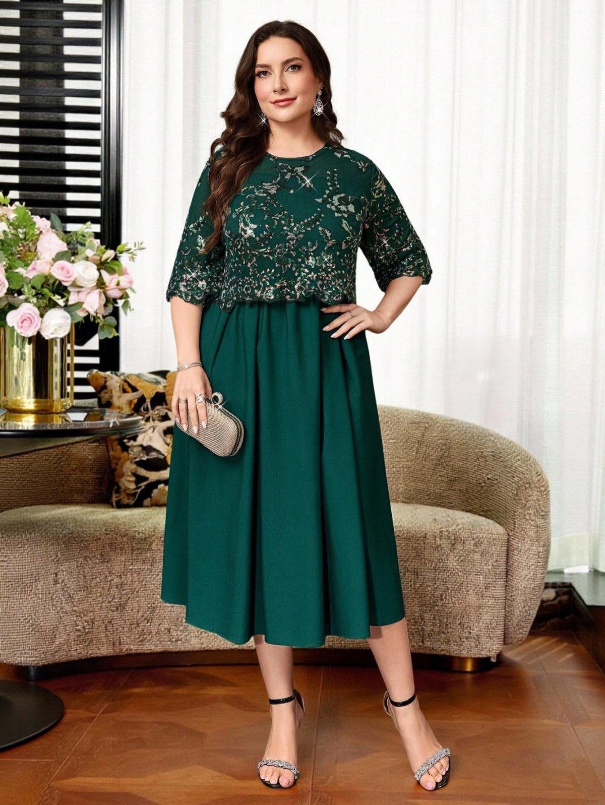A woman posing in a dark green sequined formal midi dress and silver sandals.