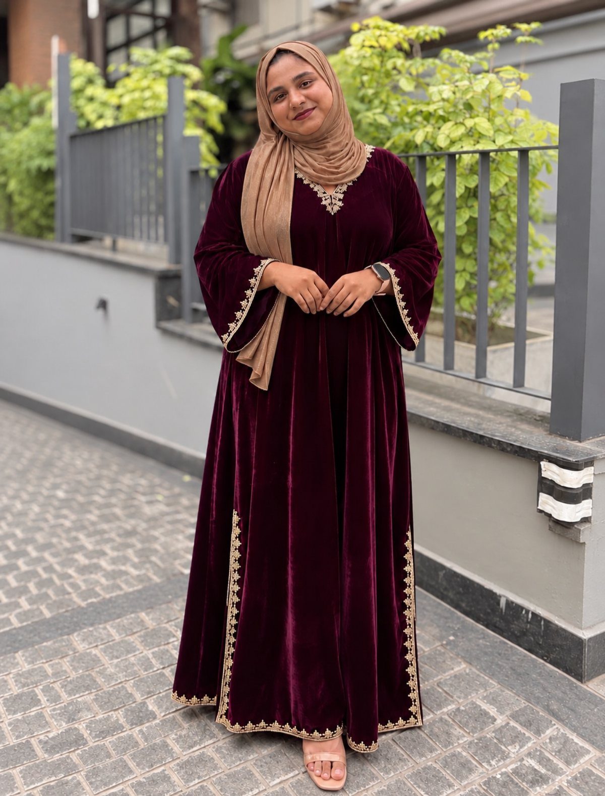 Woman in a long burgundy velvet dress with gold embroidery standing outdoors.