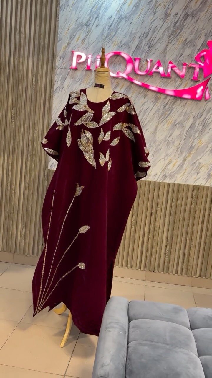 Maroon formal gown with gold sequin leaf patterns displayed on a mannequin in a boutique.