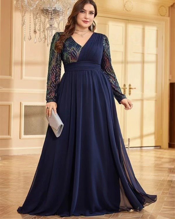 A woman posing in a navy blue long-sleeved formal gown holding a silver clutch.