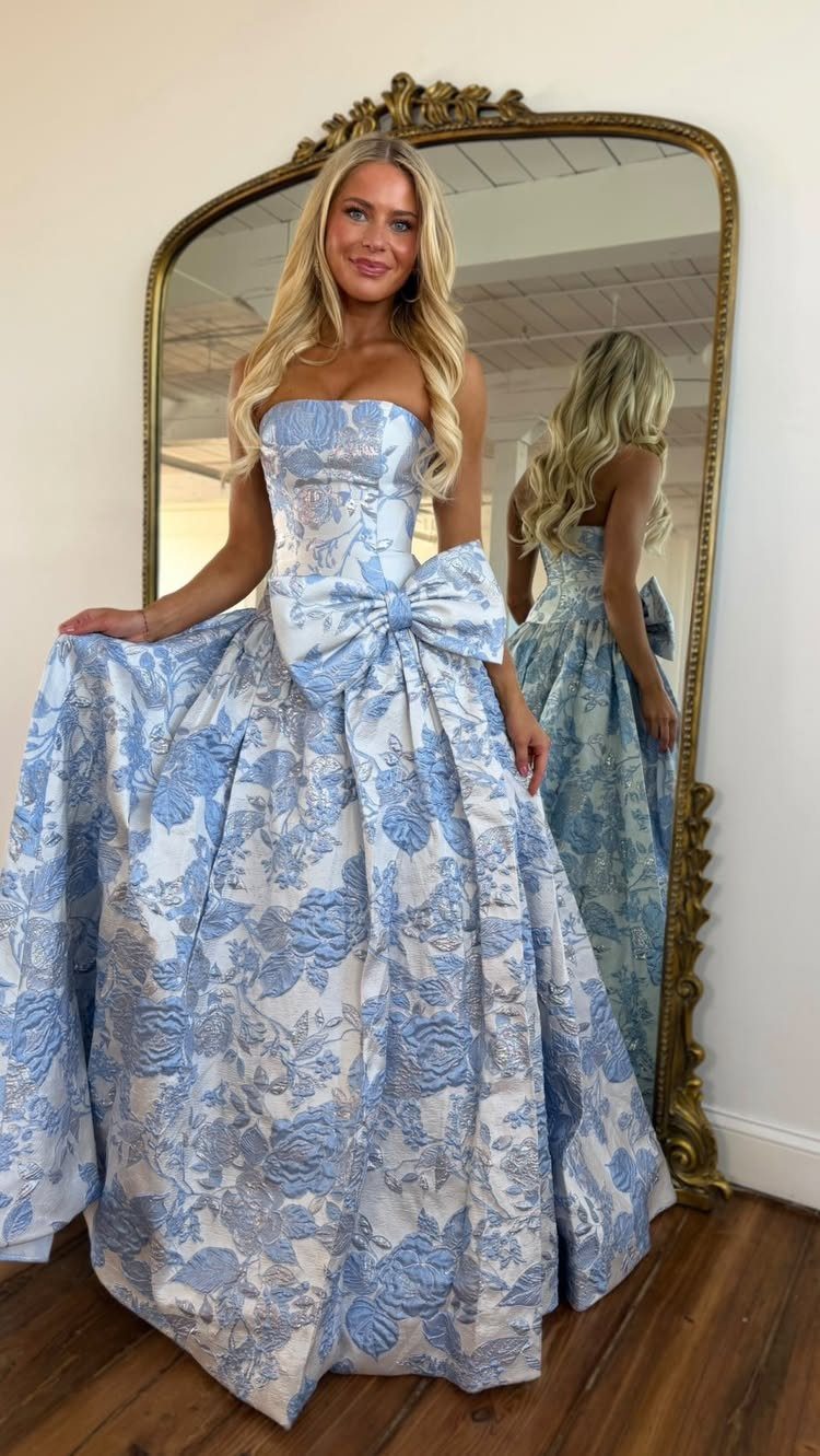 Blonde woman posing in a voluminous blue and white floral strapless ball gown.