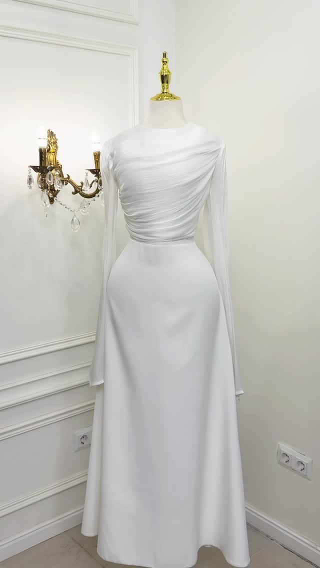 White long-sleeved gown with a draped, ruched bodice displayed on a mannequin against a white wall.