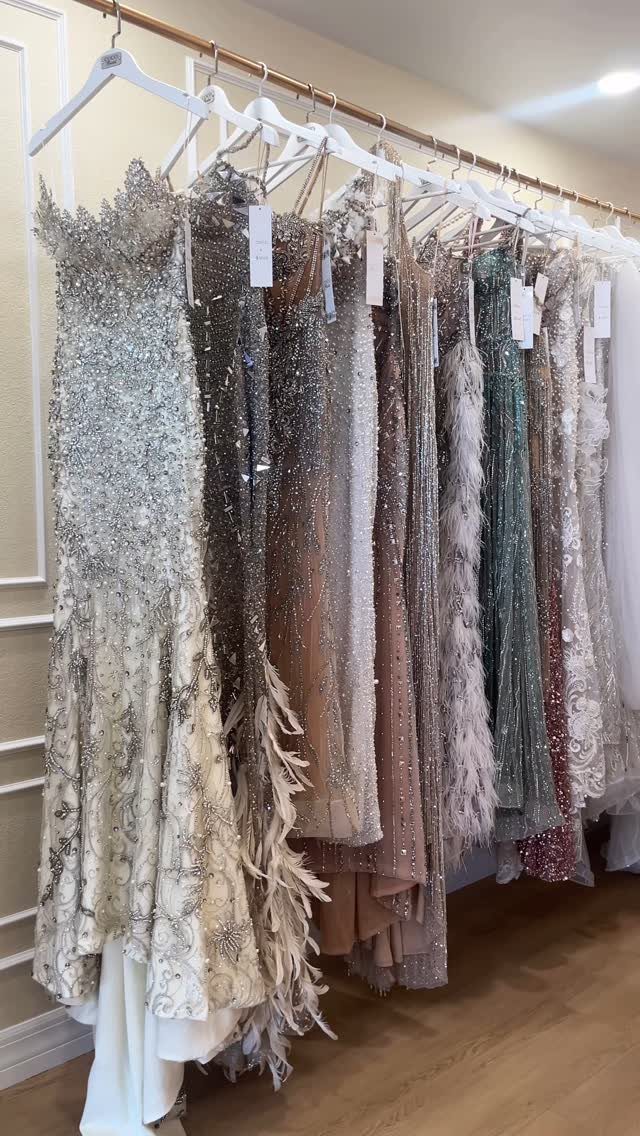 Ornate, beaded, and feathered prom dresses hanging on a gold clothing rack in a boutique.