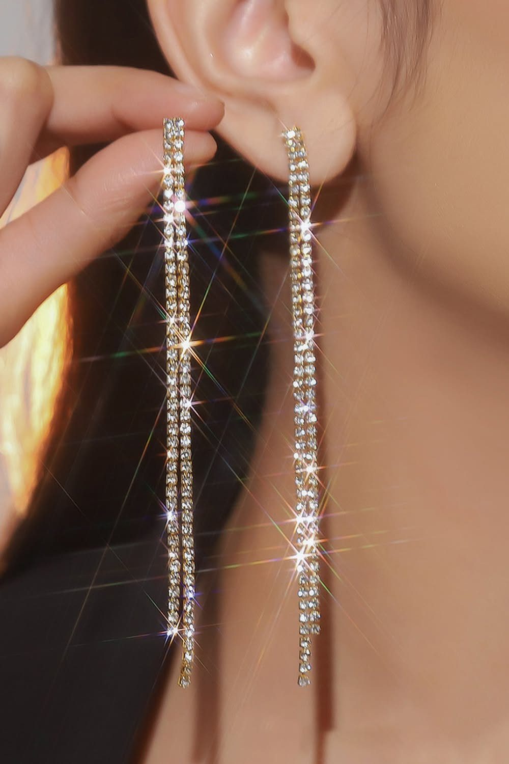 Long sparkling silver rhinestone drop earrings worn on a person's ear