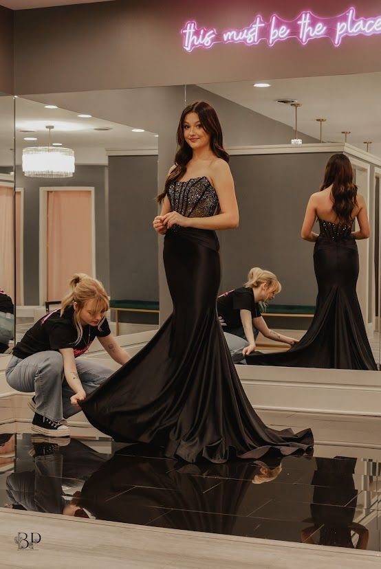 Young woman in a black prom dress being assisted by a store employee.