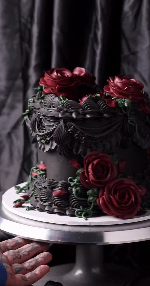 Black tiered cake decorated with large deep red roses on a silver stand.