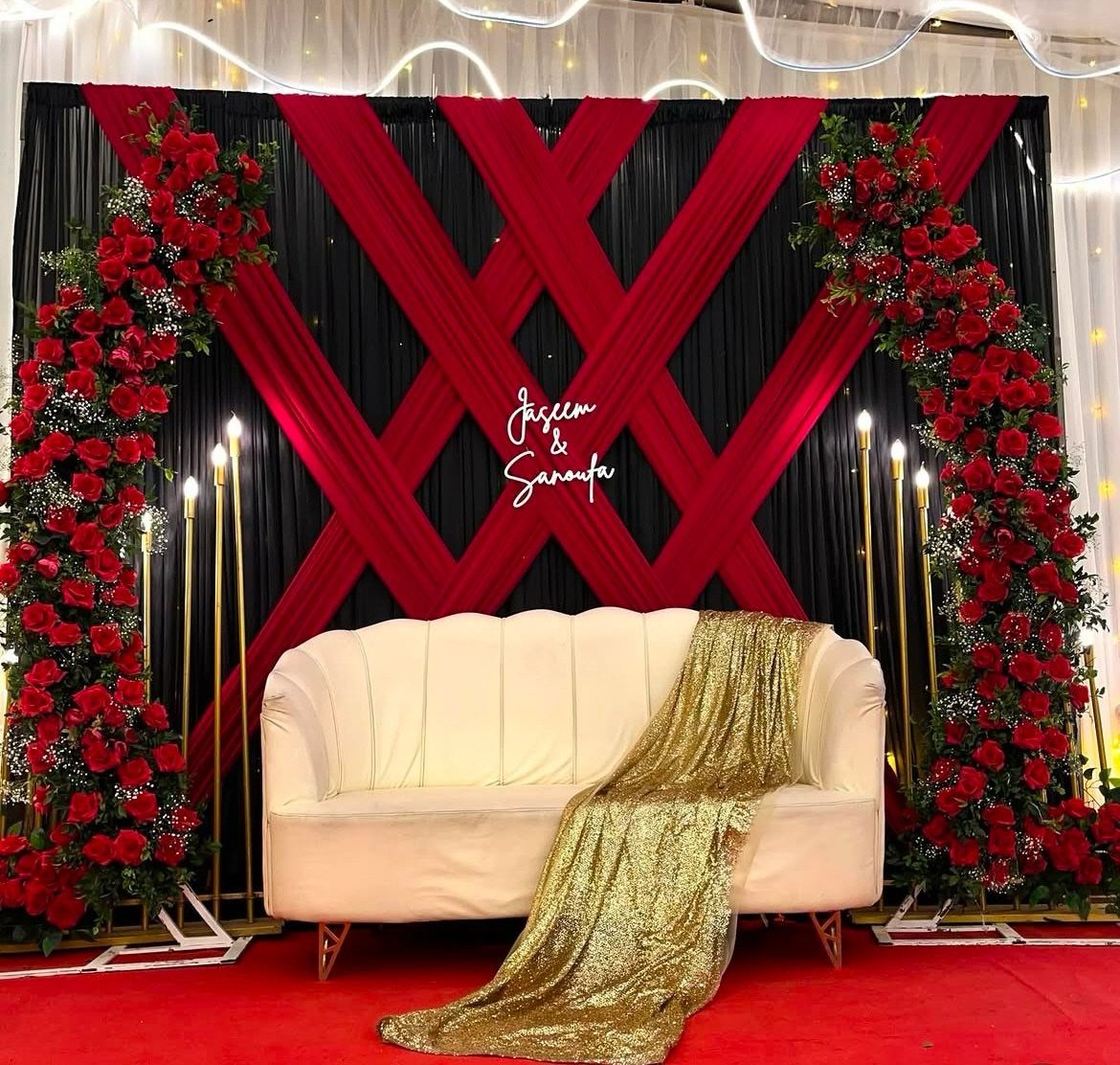 Red and black fabric backdrop with rose arrangements and a white sofa.