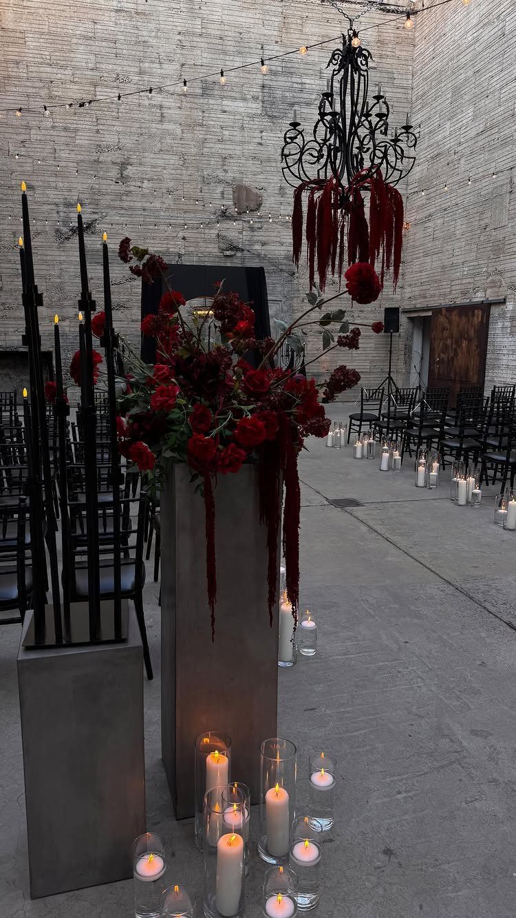Red rose floral arrangements and black candle holders decorate a concrete wedding ceremony aisle.