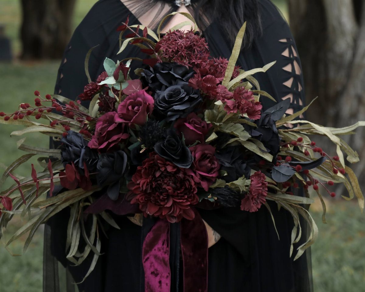 A large bouquet of dark red and black roses with greenery held by a person.