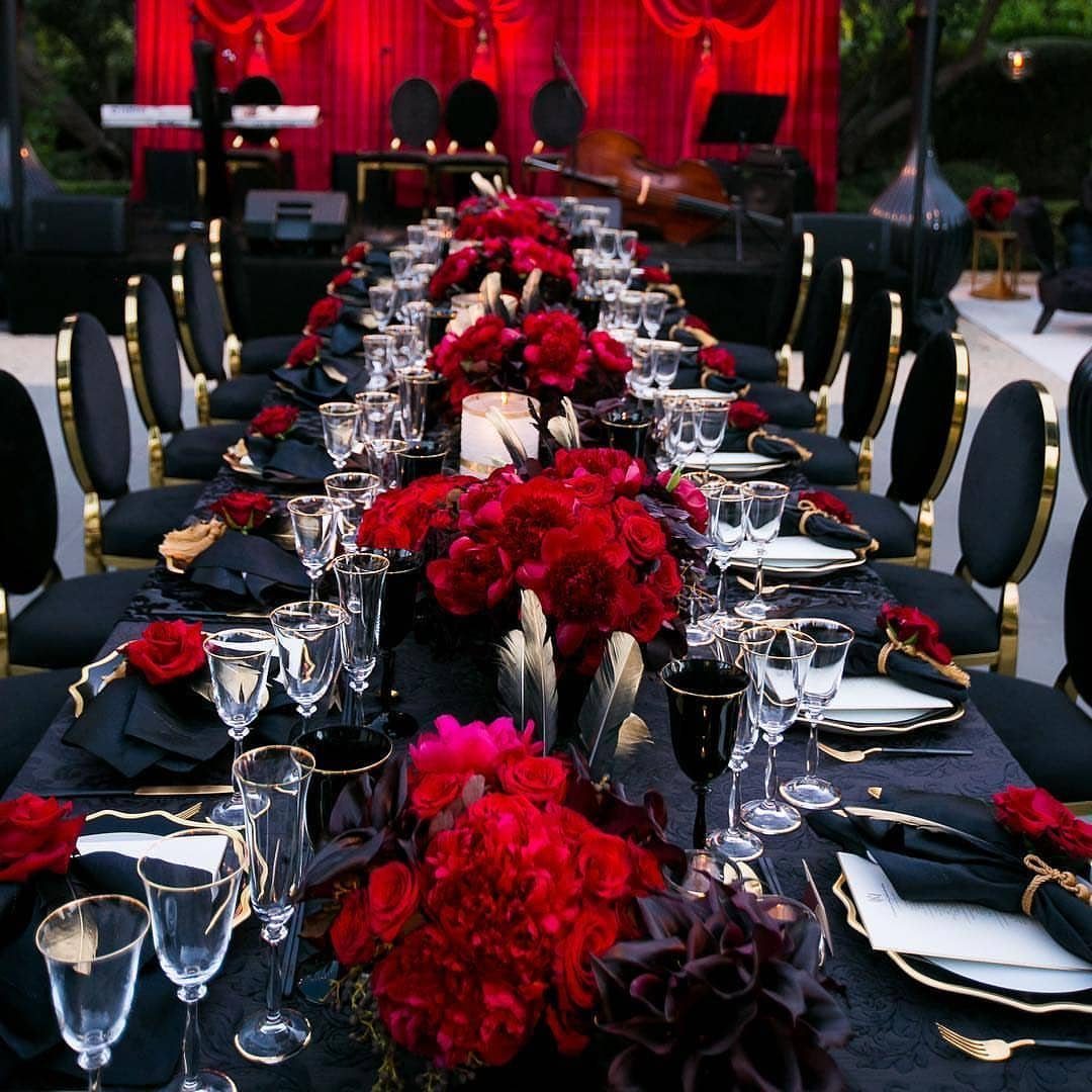 Long banquet table featuring red floral centerpieces, black linens, and elegant crystal glassware.