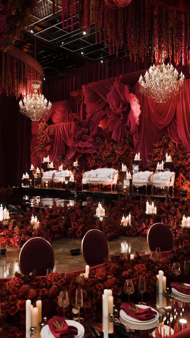 Red floral wedding decor with white sofas, crystal chandeliers, and elegant candlelit table settings.