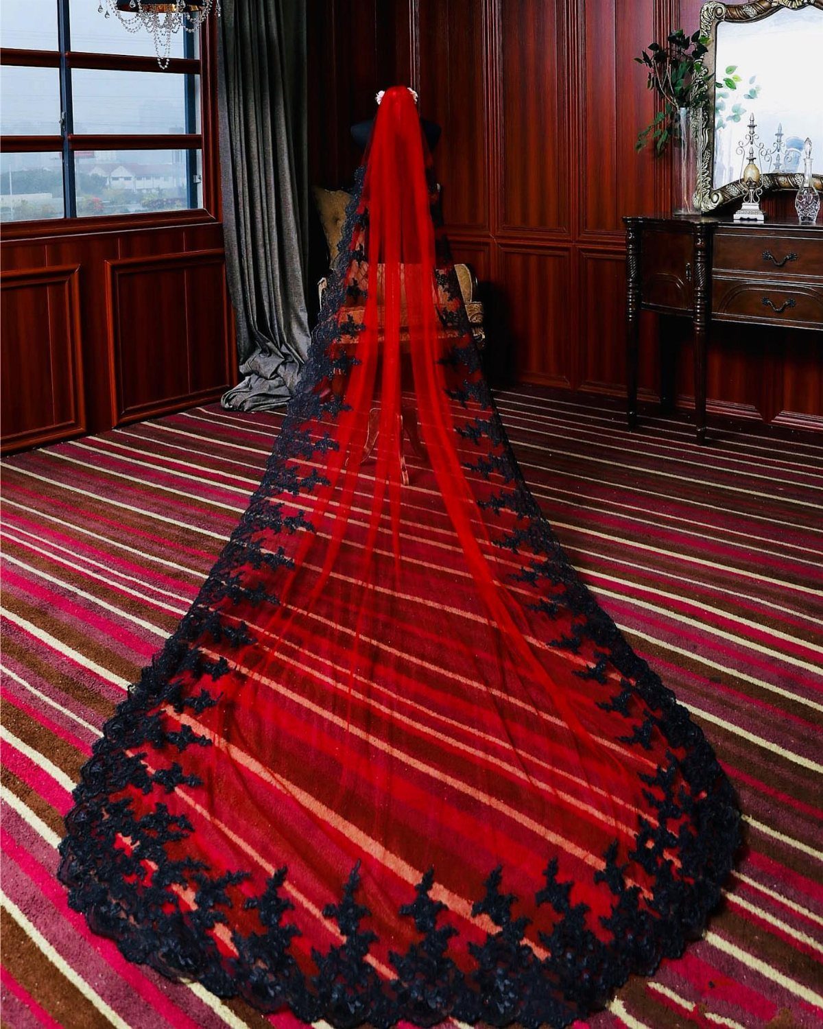 Red wedding veil with black lace trim spread across a striped carpet in a wood-paneled room.