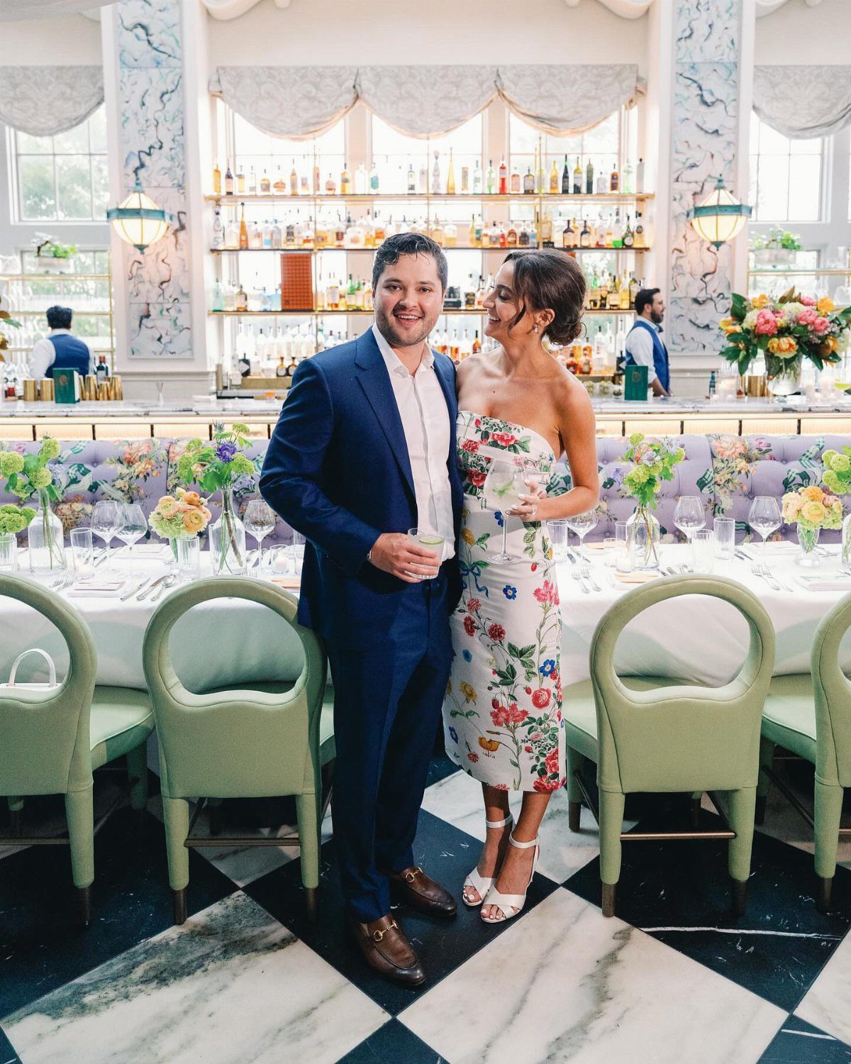 A man in a blue suit and a woman in a floral strapless midi dress posing together.