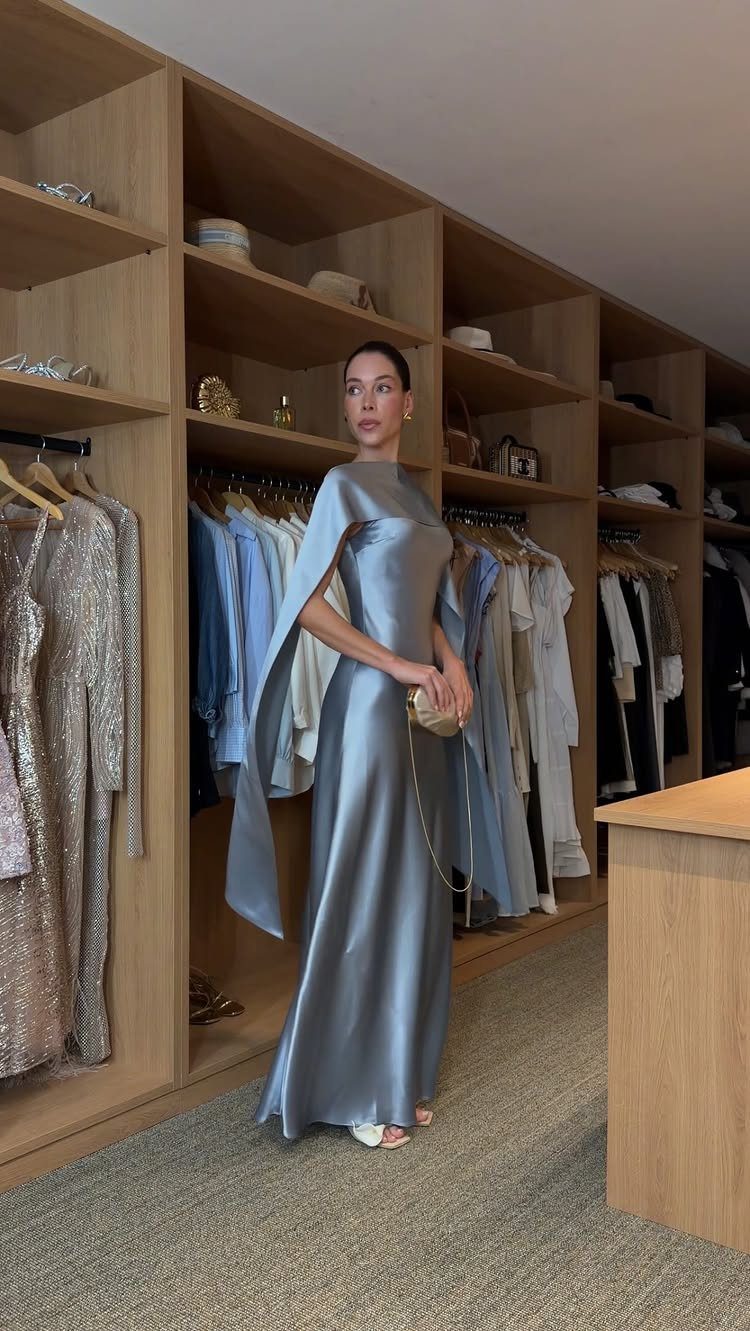 Woman in a long light blue satin gown standing in a wooden walk-in closet.