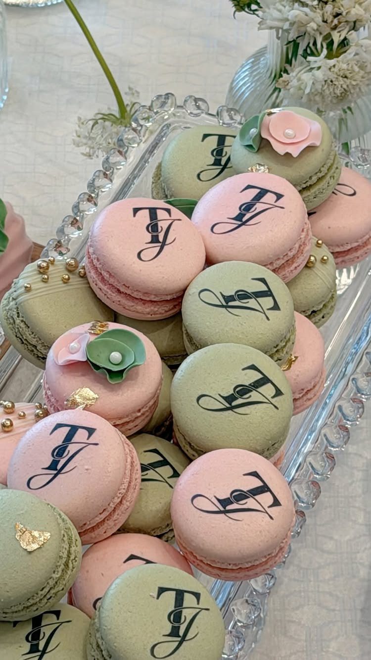 Pink and sage green macarons with black monograms on a glass platter.